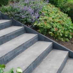 Trap van betonstenen en tegels verlijmd met steenlijm. Zijkanten afgewerkt met betonbanden 6x30 antraciet. Hoveniersbedrijf C. K. van Mourik